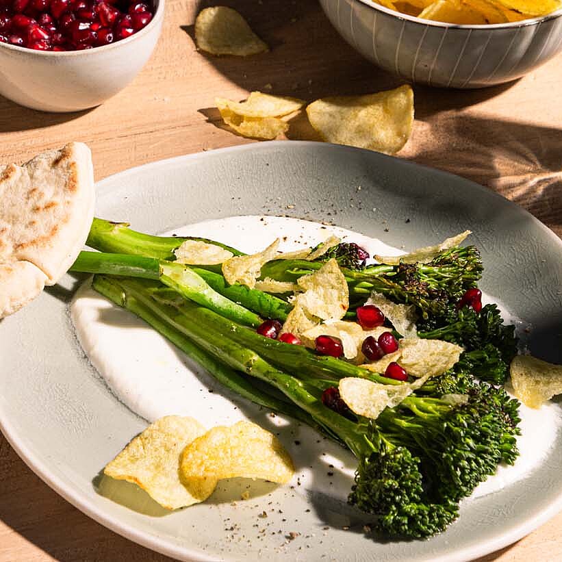 Grilled broccoli on a creamy feta cream, sprinkled with a crunchy topping and garnished with pomegranate seeds.