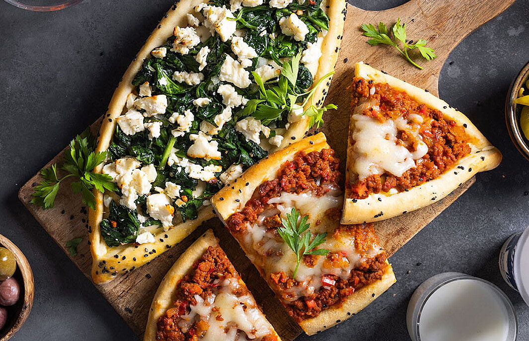 Türkische Pide mit Hackfleisch und Spinat, angerichtet auf einem Holzbrett