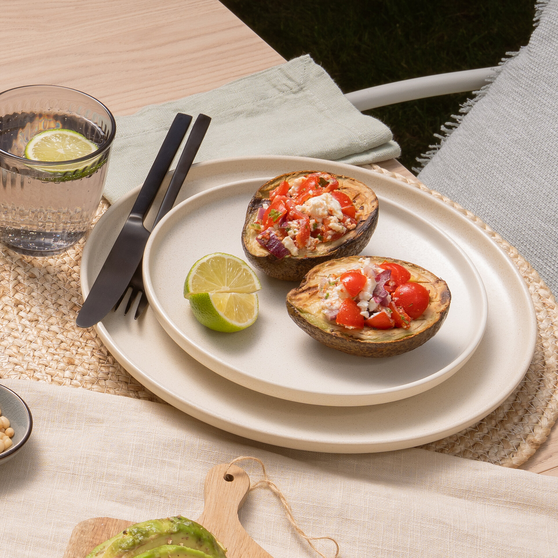 Summer table setting with grilled avocado, fresh tomato and feta salsa, bread, limes, and olives.