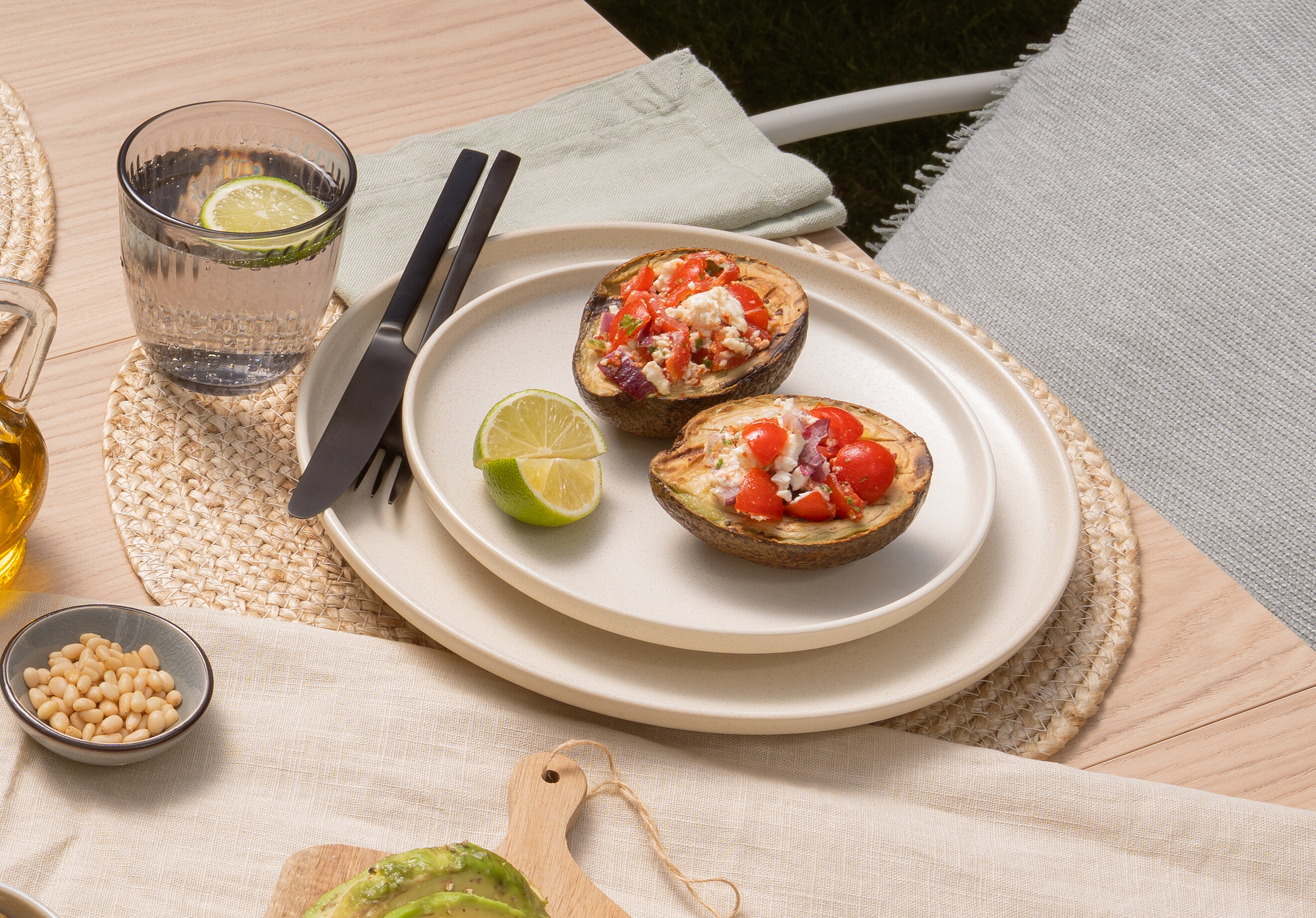 Summer table setting with grilled avocado, fresh tomato and feta salsa, bread, limes, and olives.
